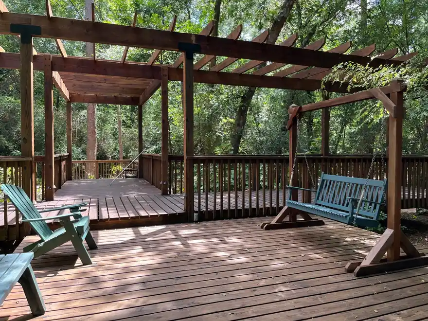 Freshly stained deck with a pergola and porch swing under shade trees