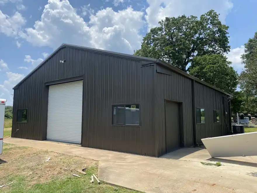 Metal shop building painted black with a white roll-up door
