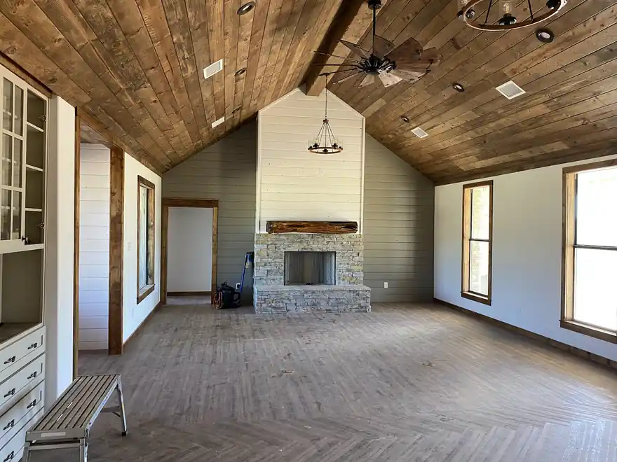 Vaulted room with a stained tongue-and-groove ceiling, painted shiplap walls and a stone fireplace