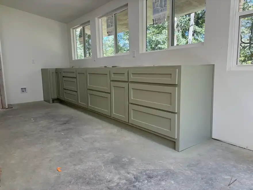 Sage-green base cabinets freshly sprayed in a new build with a bare concrete floor