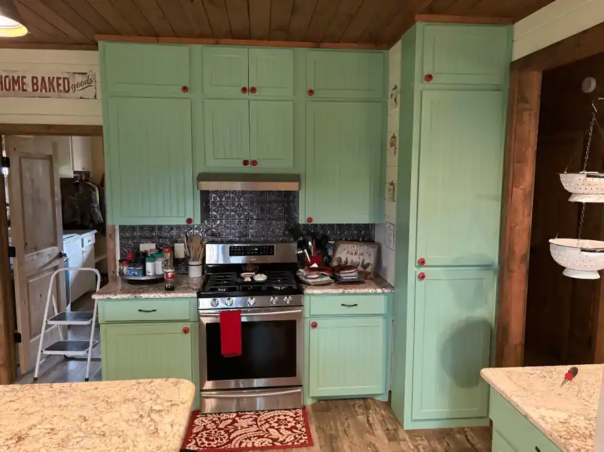Mint-green kitchen cabinets with red knobs beside a stainless range