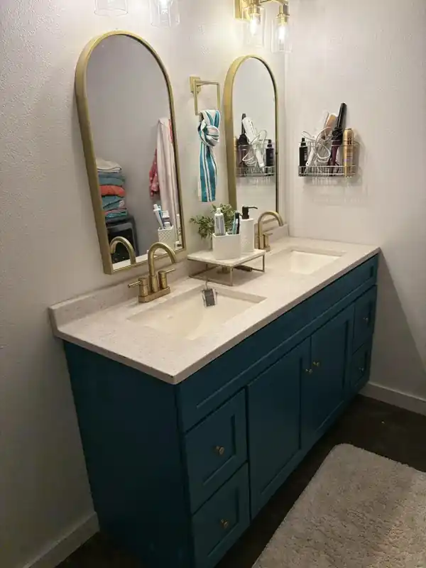 Bathroom vanity painted deep teal under brass mirrors